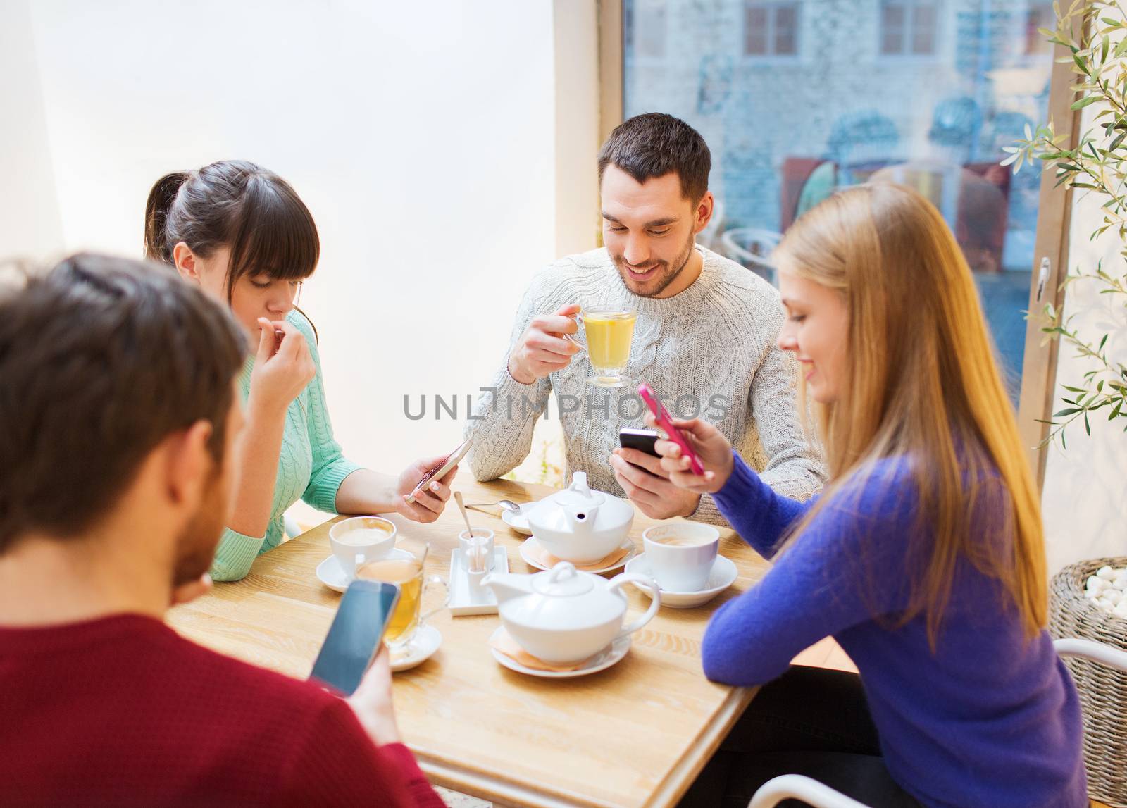 people, leisure, friendship and technology concept - group of happy friends with smartphones meeting at cafe and drinking tea