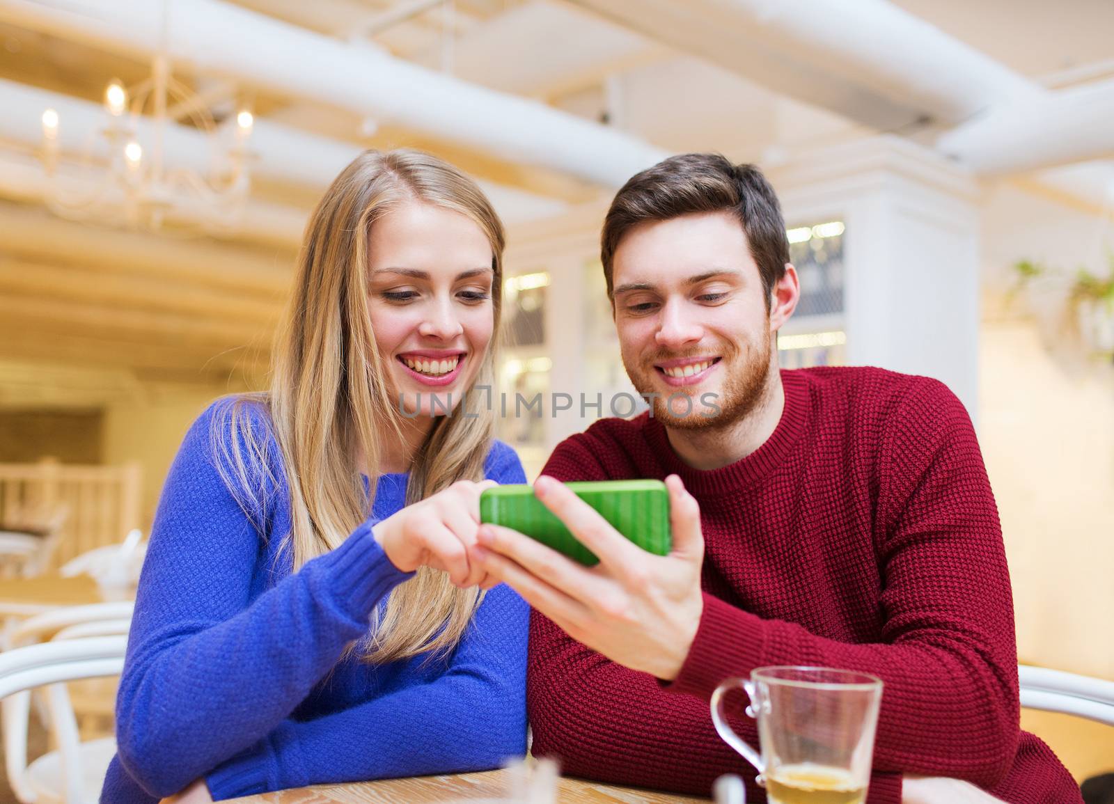 people, leisure, friendship and technology concept - smiling couple with smartphone meeting and drinking tea at cafe