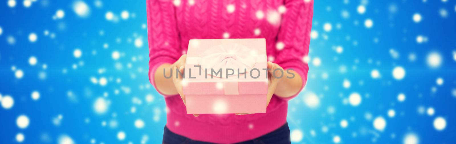 christmas, holidays and people concept - close up of woman in pink sweater holding gift box blue snowy background