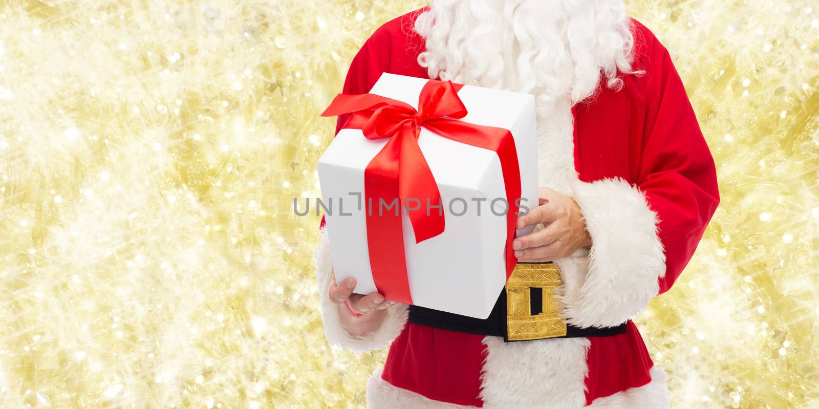 christmas, holidays and people concept - close up of santa claus with gift box over yellow lights background