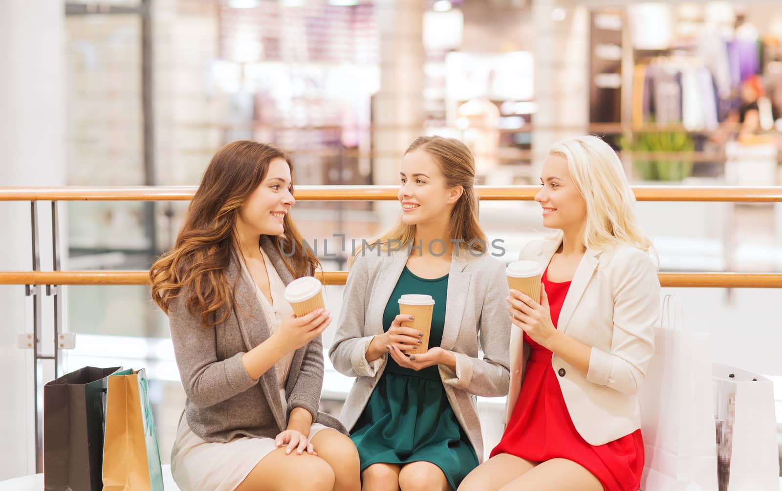 sale, consumerism and people concept - happy young women with shopping bags and coffee paper cups in mall