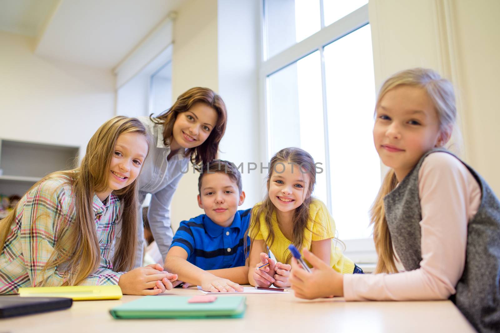 education, elementary school, learning and people concept - teacher helping school kids writing test in classroom