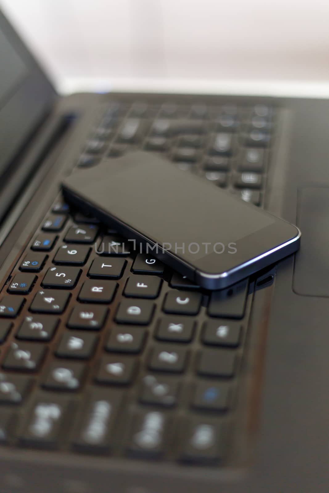 Close up detailed view of a black laptop pc with a black smart phone on.