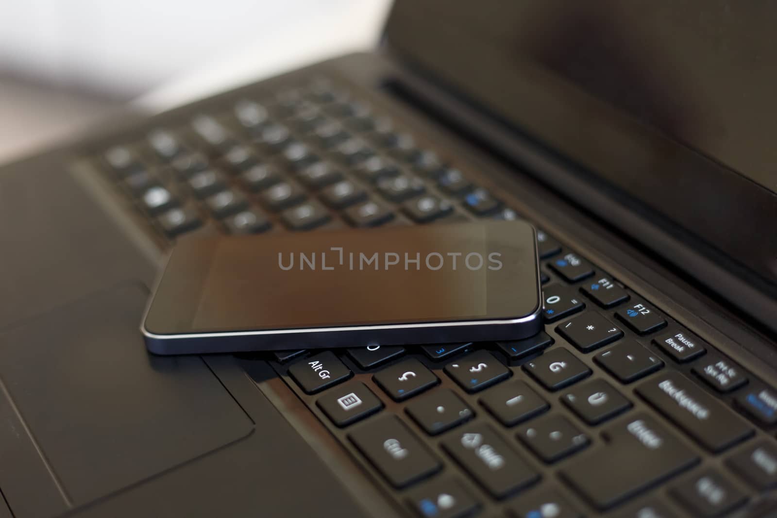 Close up detailed view of a black laptop pc with a black smart phone on.