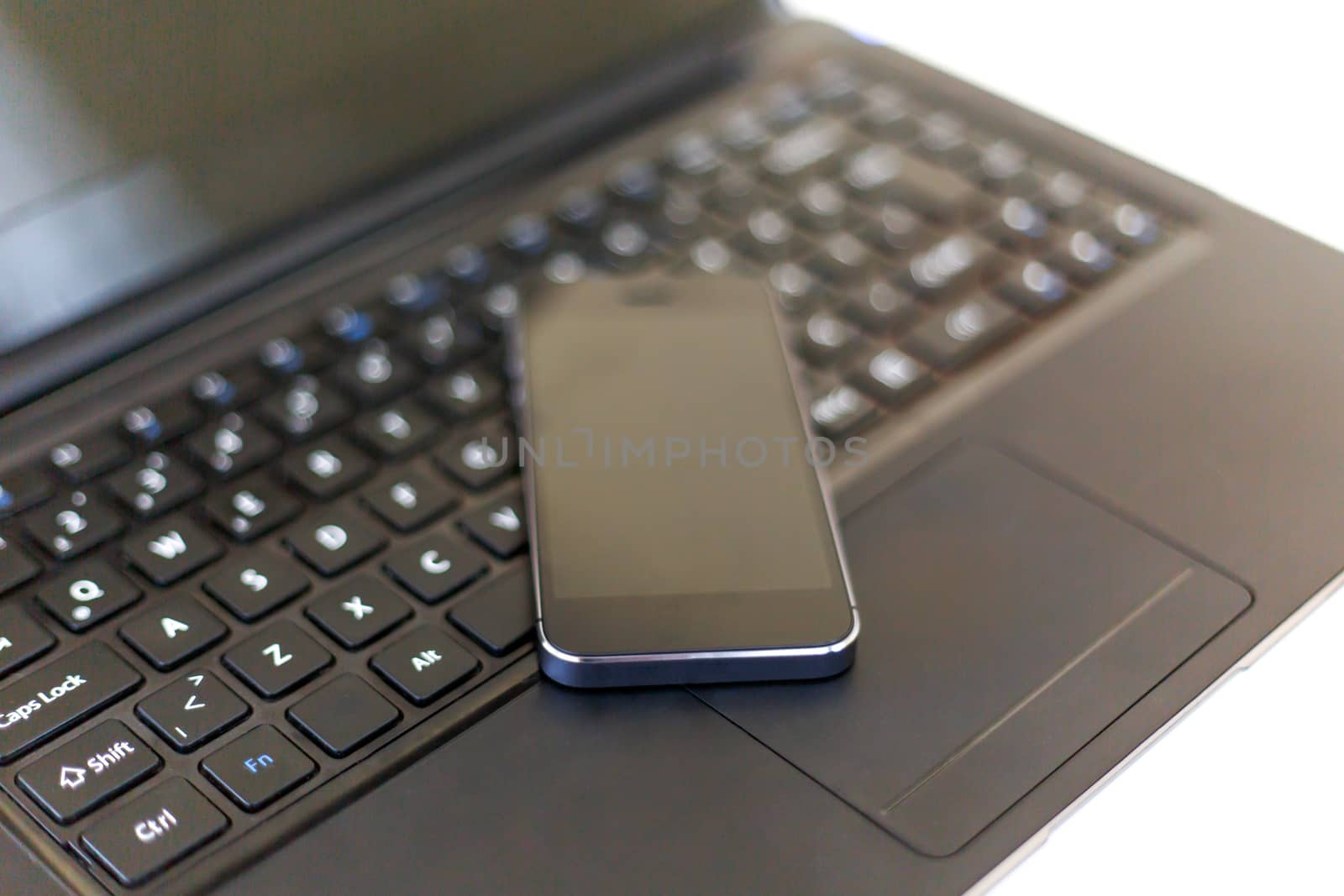 Close up detailed view of a black laptop pc with a black smart phone on.