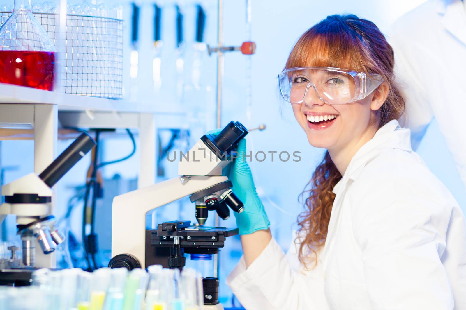 Attractive young female research scientist having fun while looking at the microscope slide in the life science laboratory. Not taking yourself to serious.