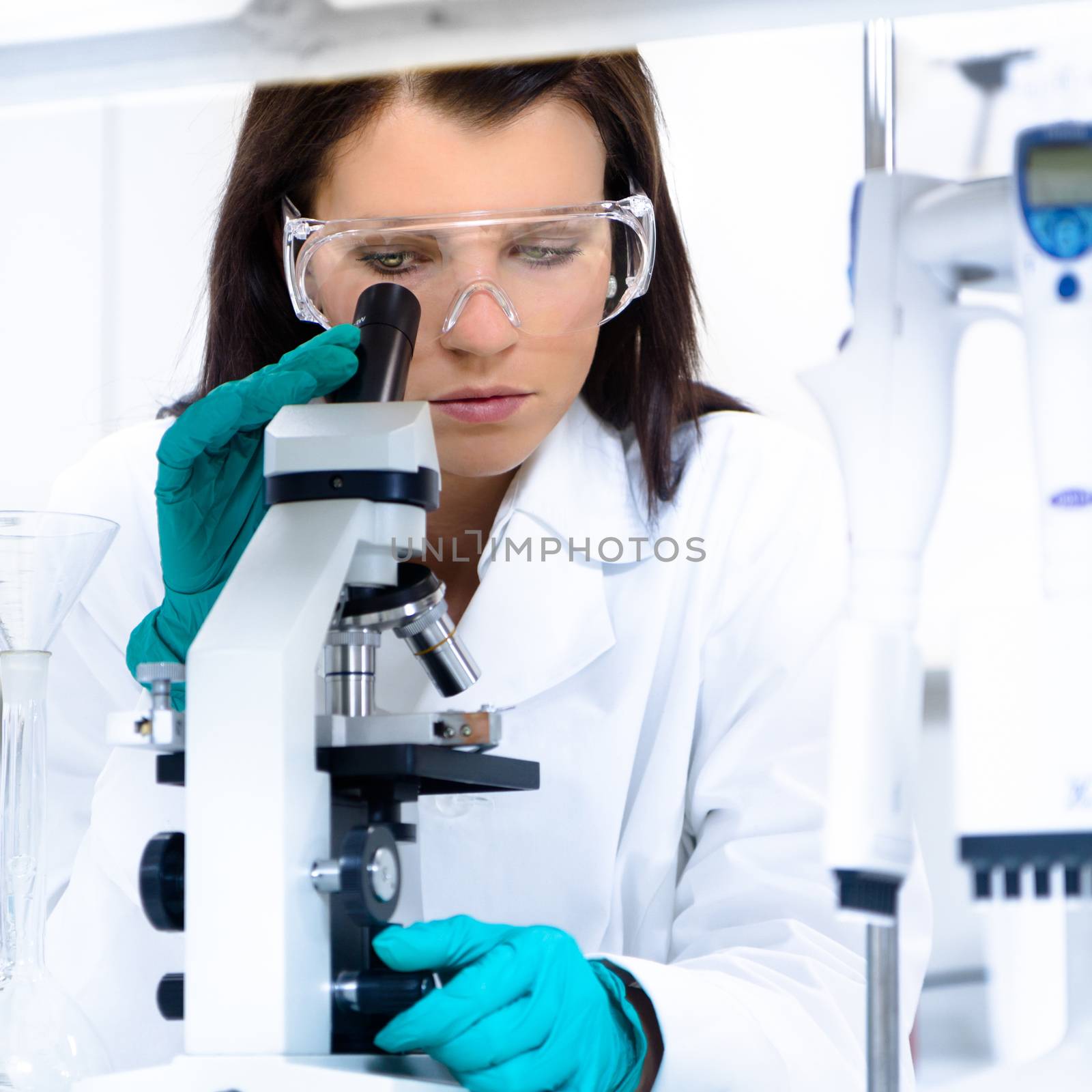 Attractive young PhD student scientist looking at the microscope slide in the life science research laboratory. Biochemistry, genetics, forensics, microbiology ..