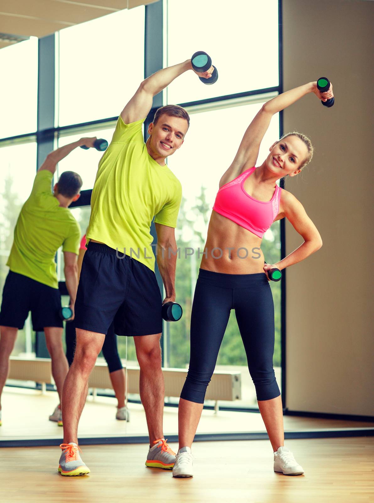 smiling man and woman with dumbbells in gym by dolgachov