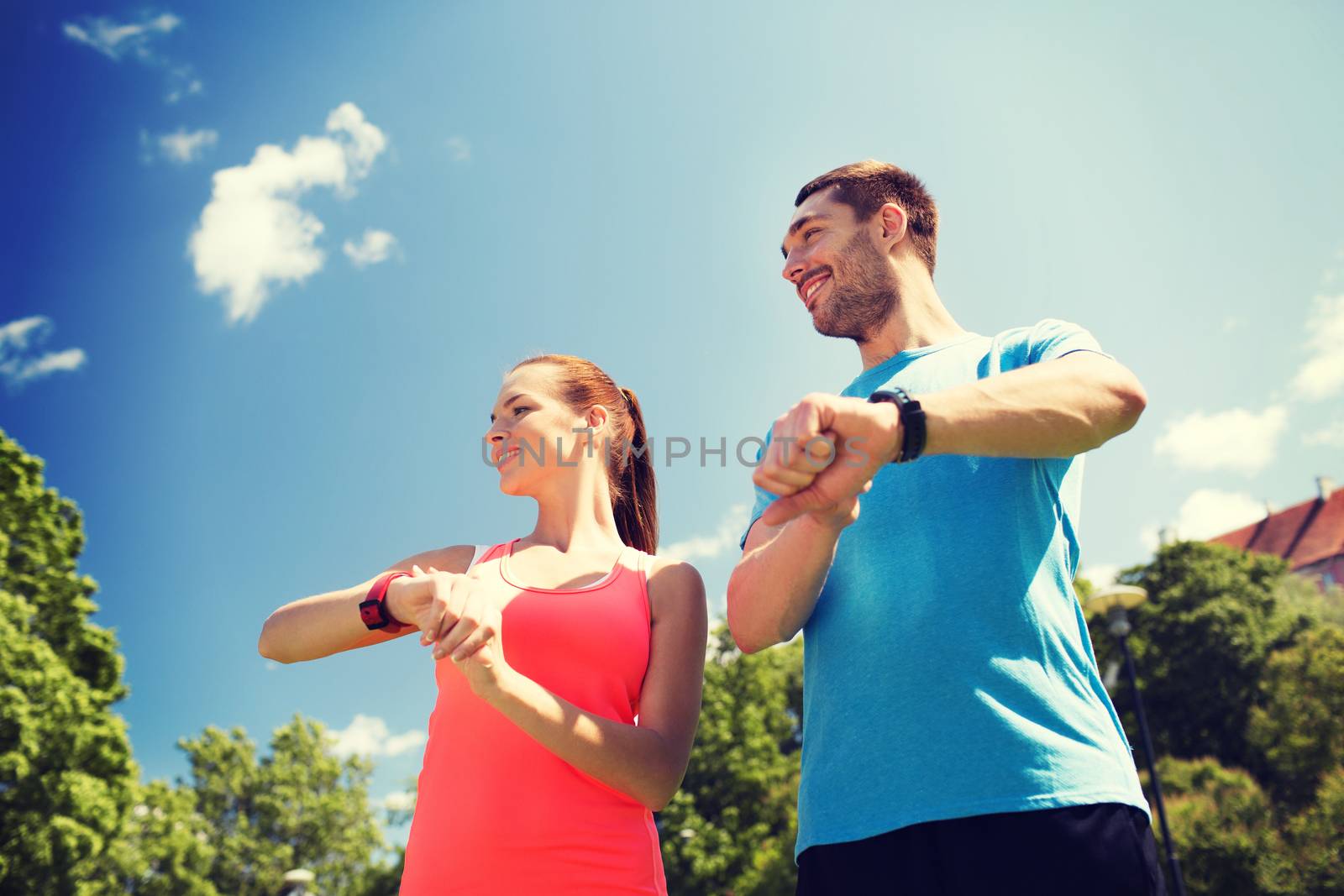 fitness, sport, training, technology and lifestyle concept - two smiling people with heart rate watches outdoors