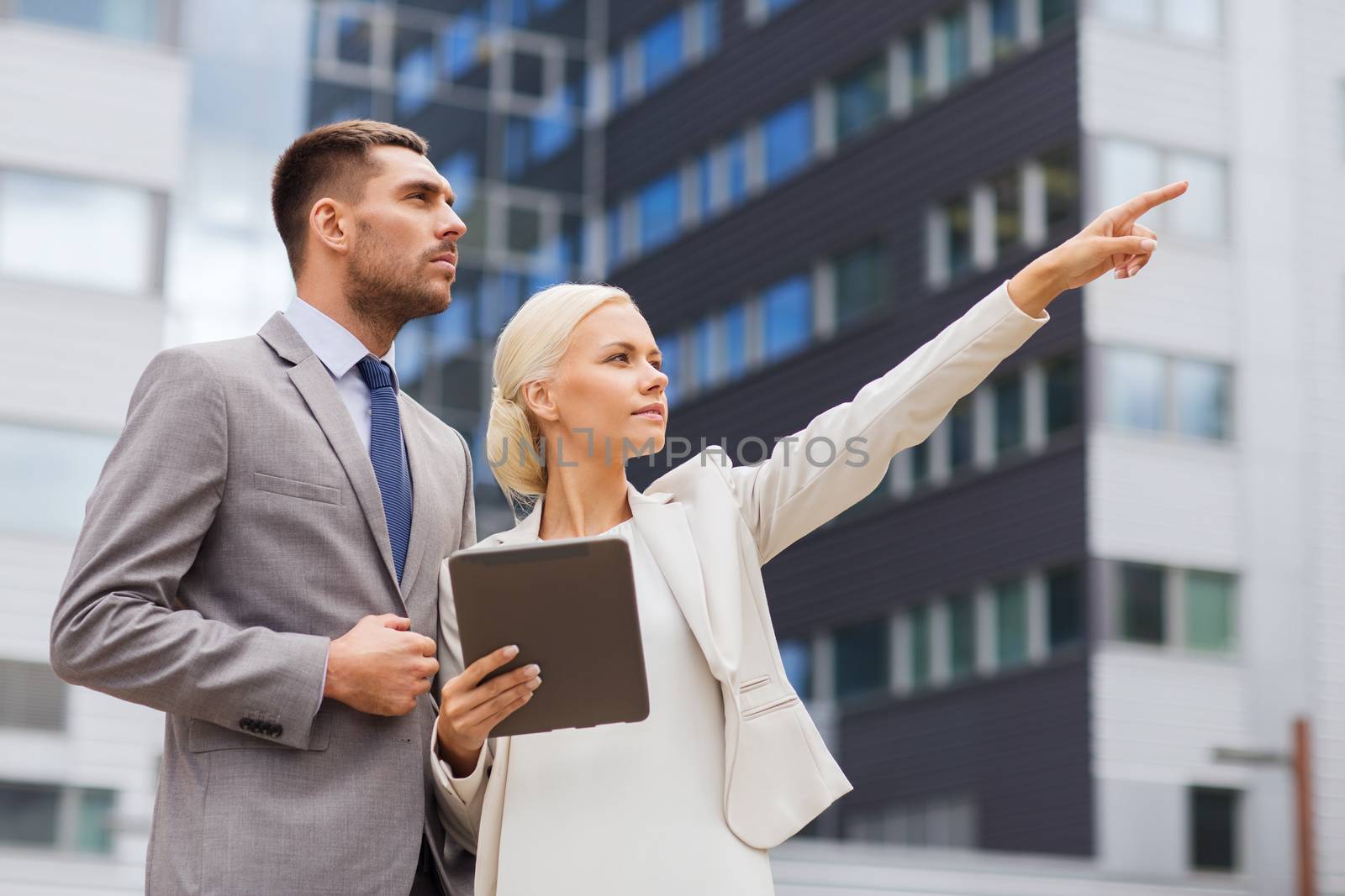 business, partnership, technology and people concept - serious businessman and businesswoman with tablet pc computer over office building