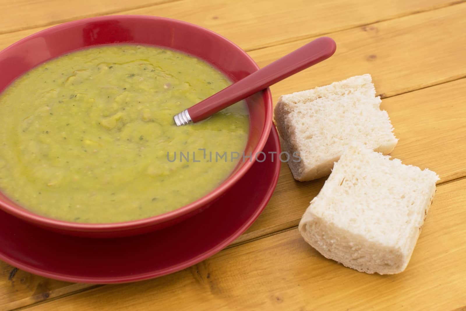 Green pea and ham soup in a red bowl, served with chunks of fresh white bread