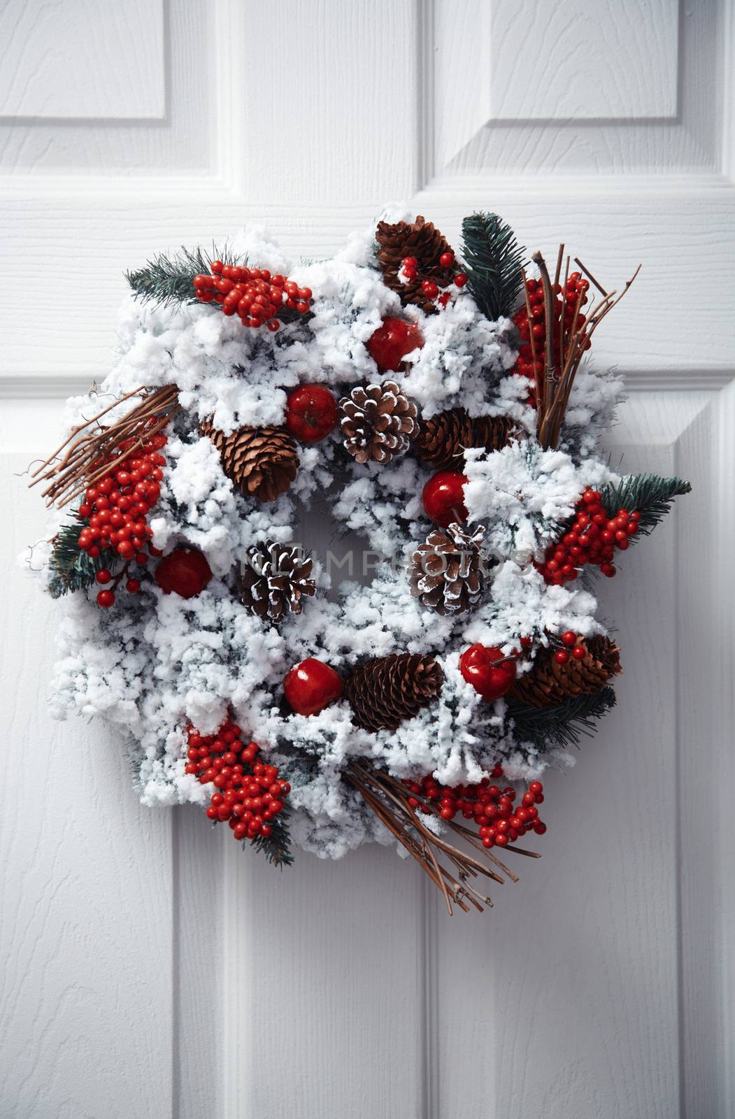 White front door decorated by Christmas wreath. Vertical photo