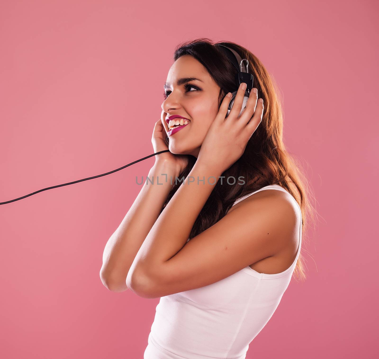 Young woman listening to music over a pink background.
