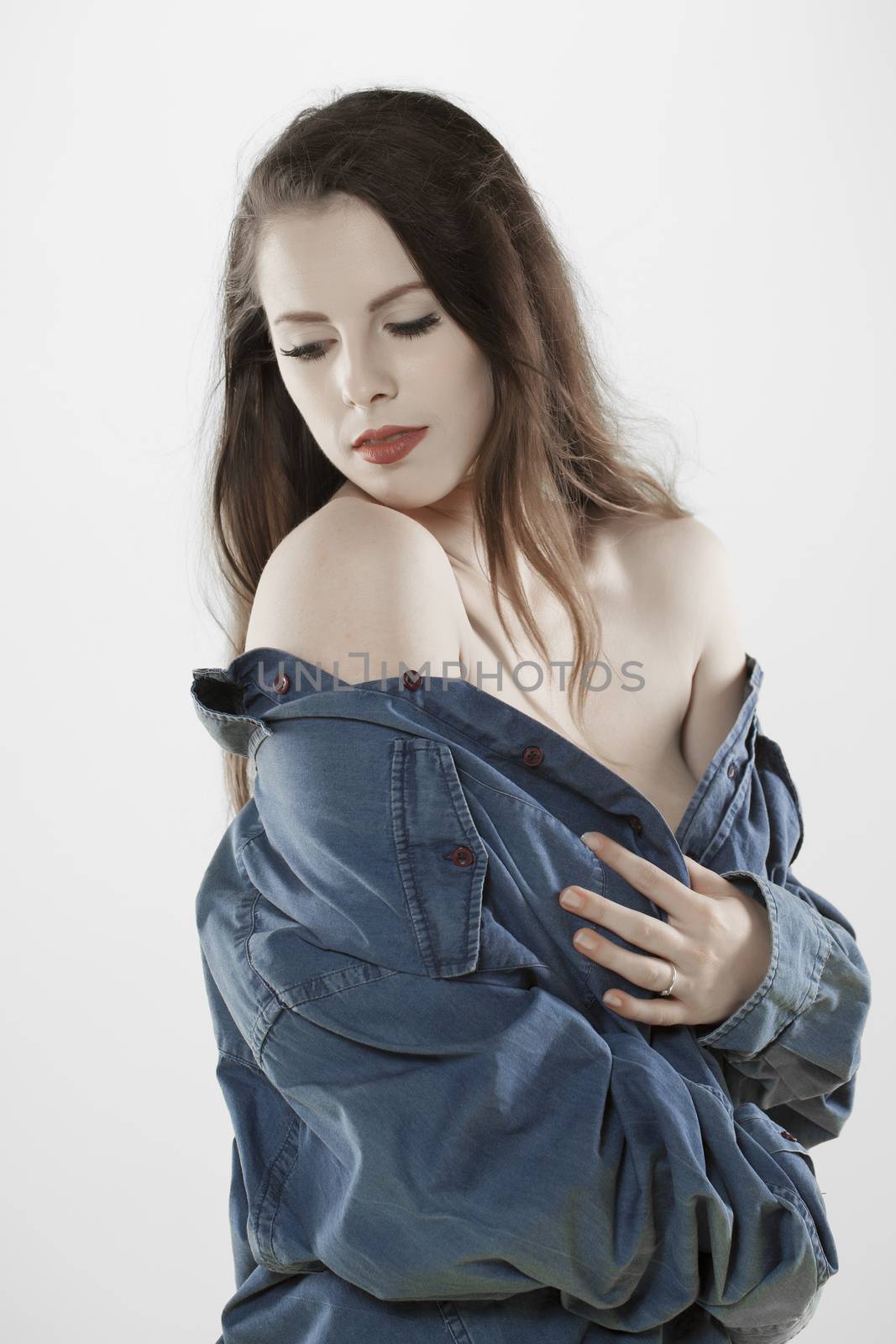 A beautiful fair skinned woman wearing a manes denim shirt over a light background.