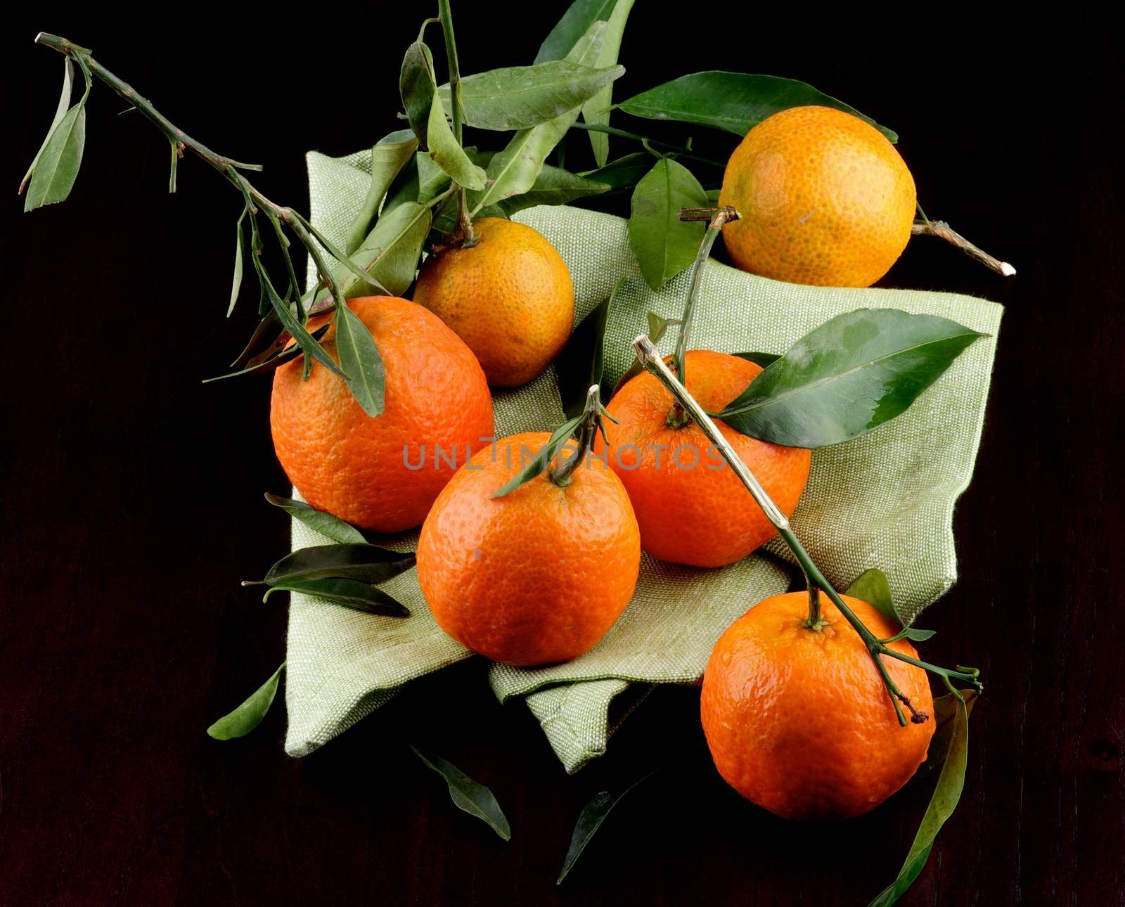 Heap of Ripe Tangerines with Leafs on Green Napkin closeup on Dark Wooden background