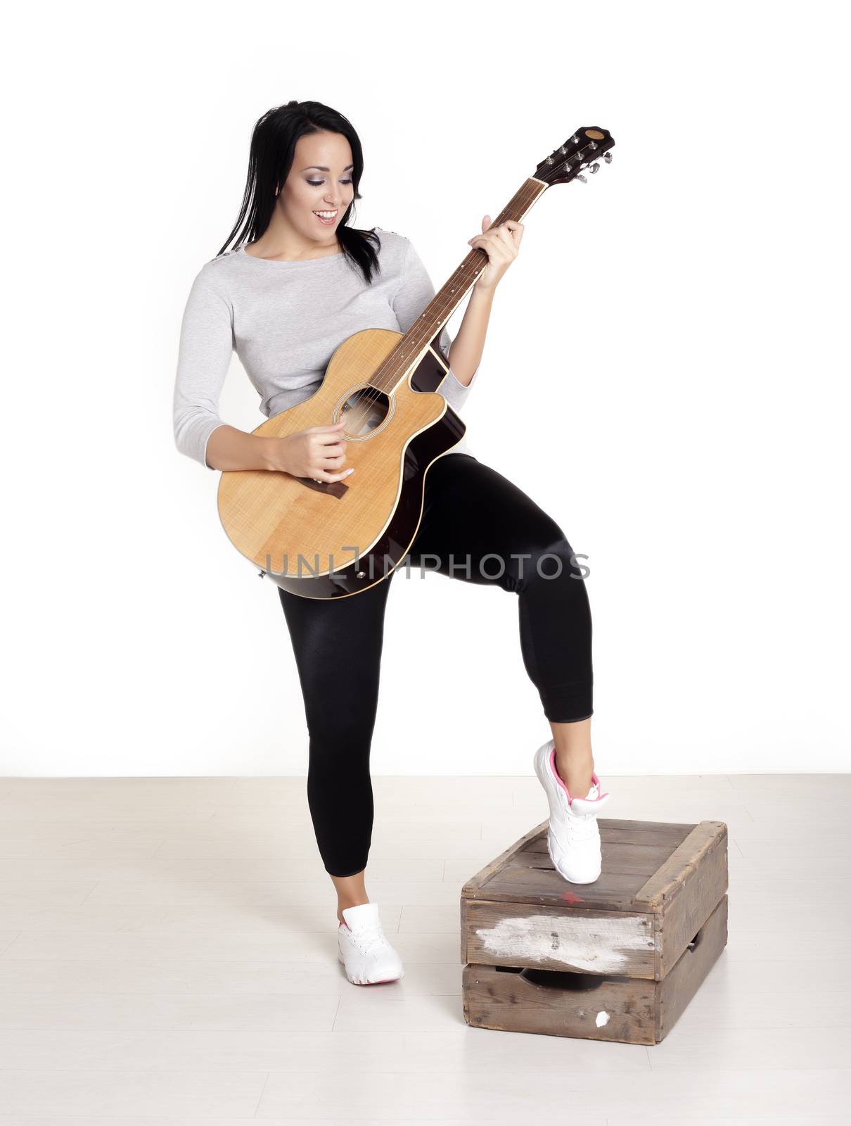 Young female busker sitting on a wooden box playing her guitar for money.