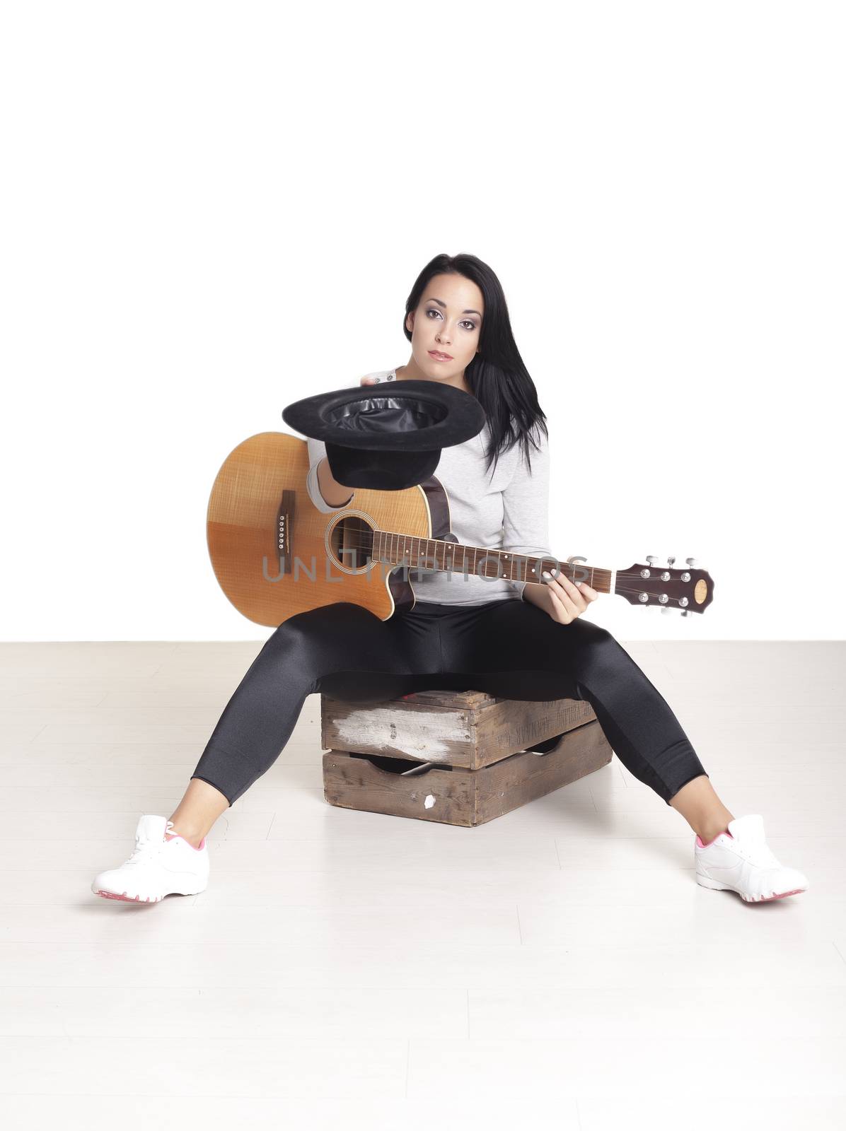 Young female busker sitting on a wooden box playing her guitar for money.