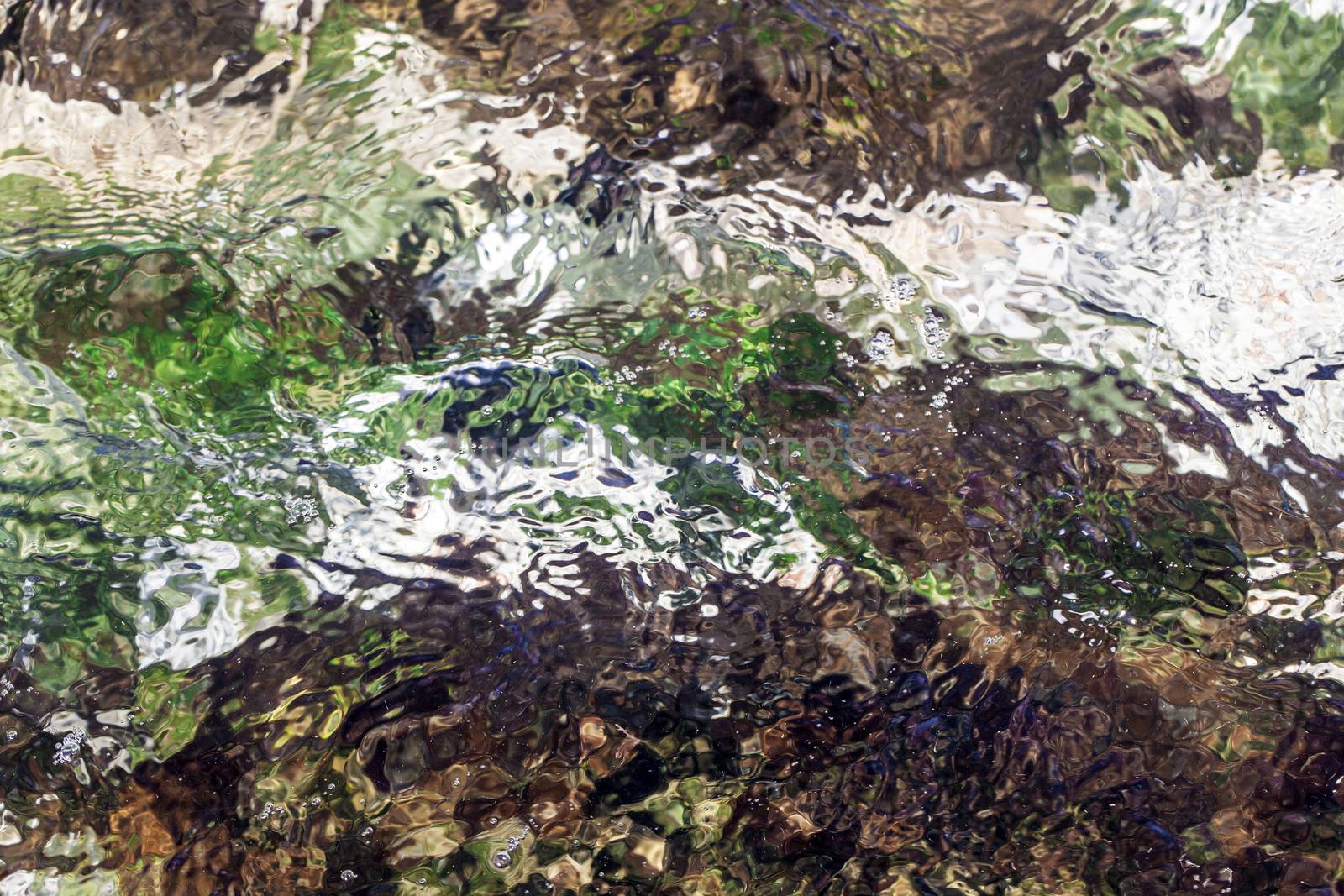 Water flowing over different coloured rocks as a abstract water background.
