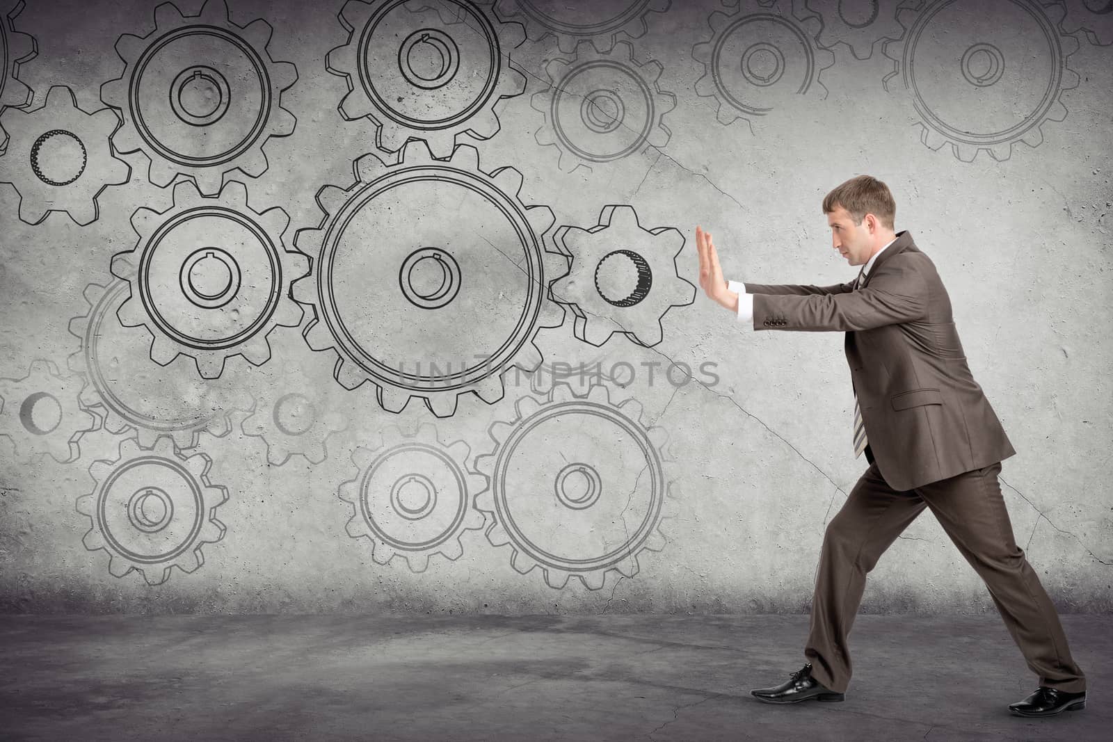 Businessman pushing cog wheel on abstract background