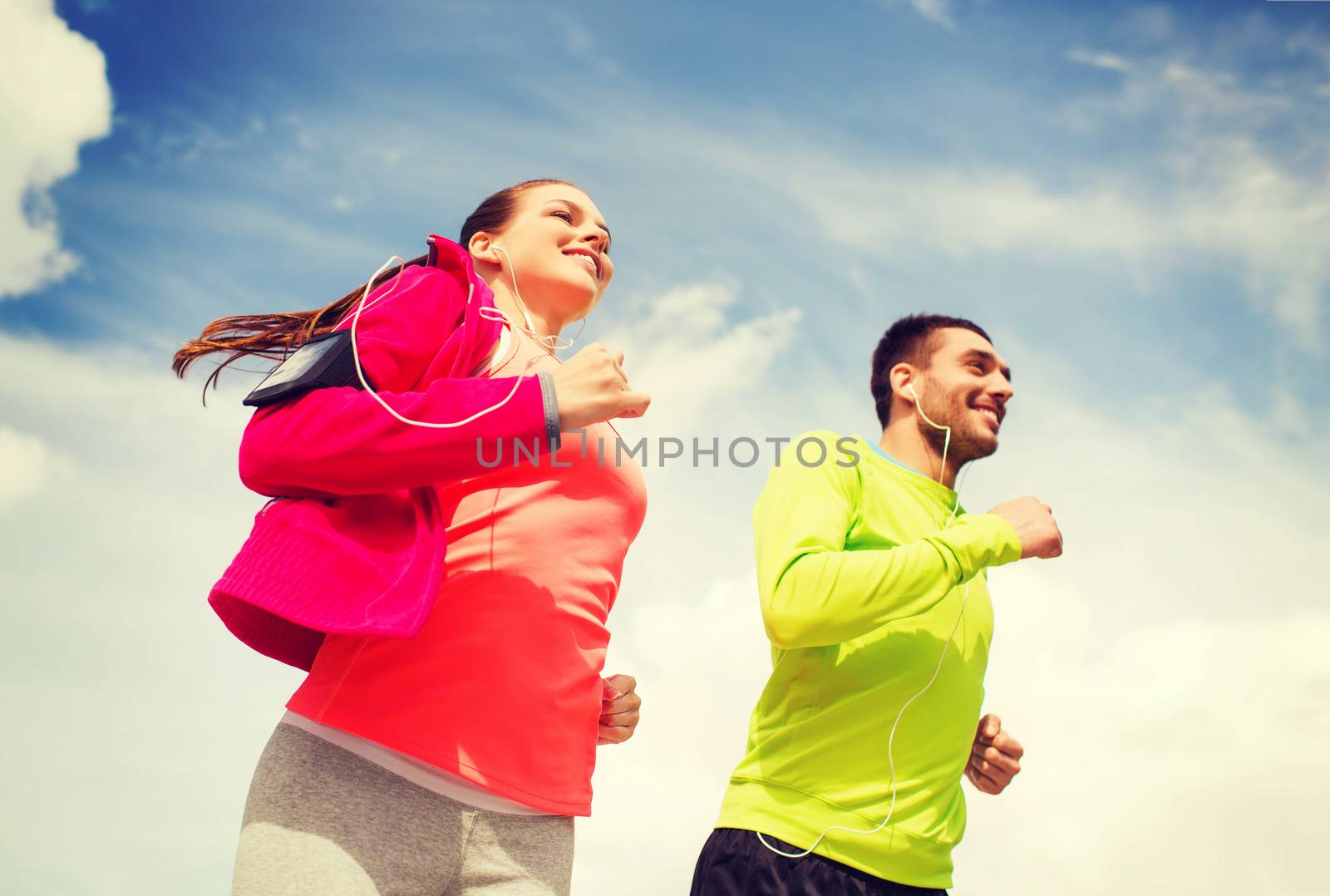 fitness, sport, friendship and lifestyle concept - smiling couple with earphones running outdoors