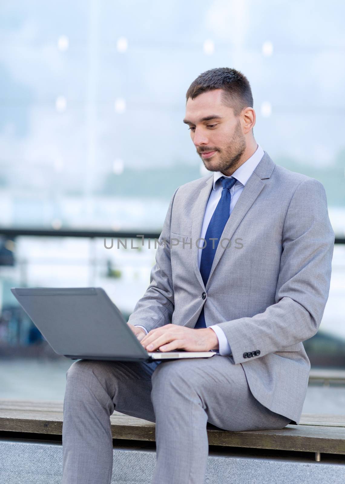 business, education, technology and people concept - businessman working with laptop computer on city street