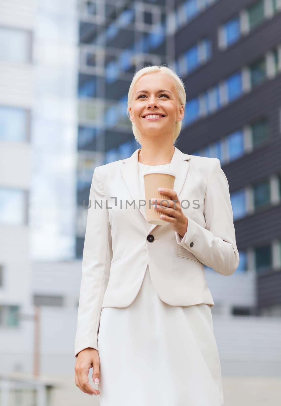business, hot drinks and people and concept - young smiling businesswoman with paper coffee cup over office building