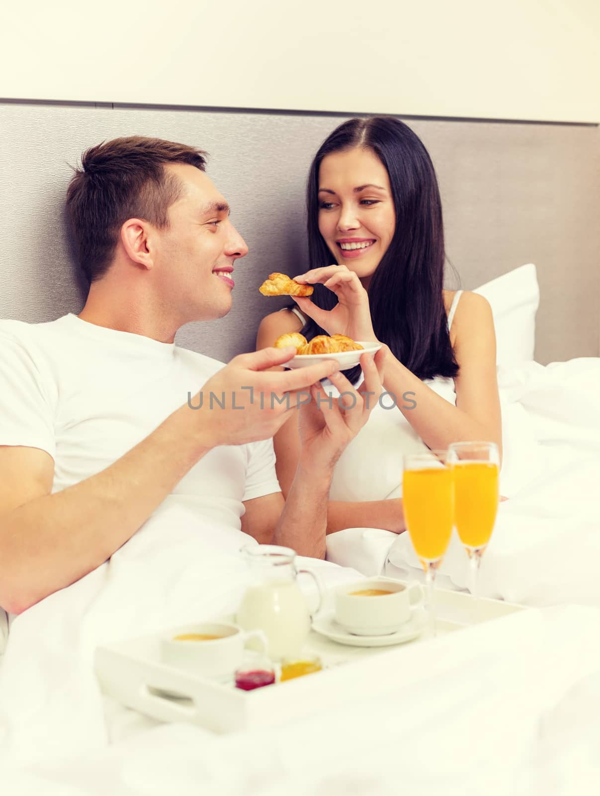 hotel, travel, relationships and happiness concept - smiling couple having breakfast in bed in hotel room