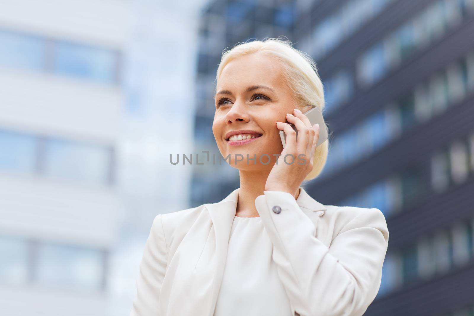 business, technology and people concept - smiling businesswoman with smartphone talking over office building