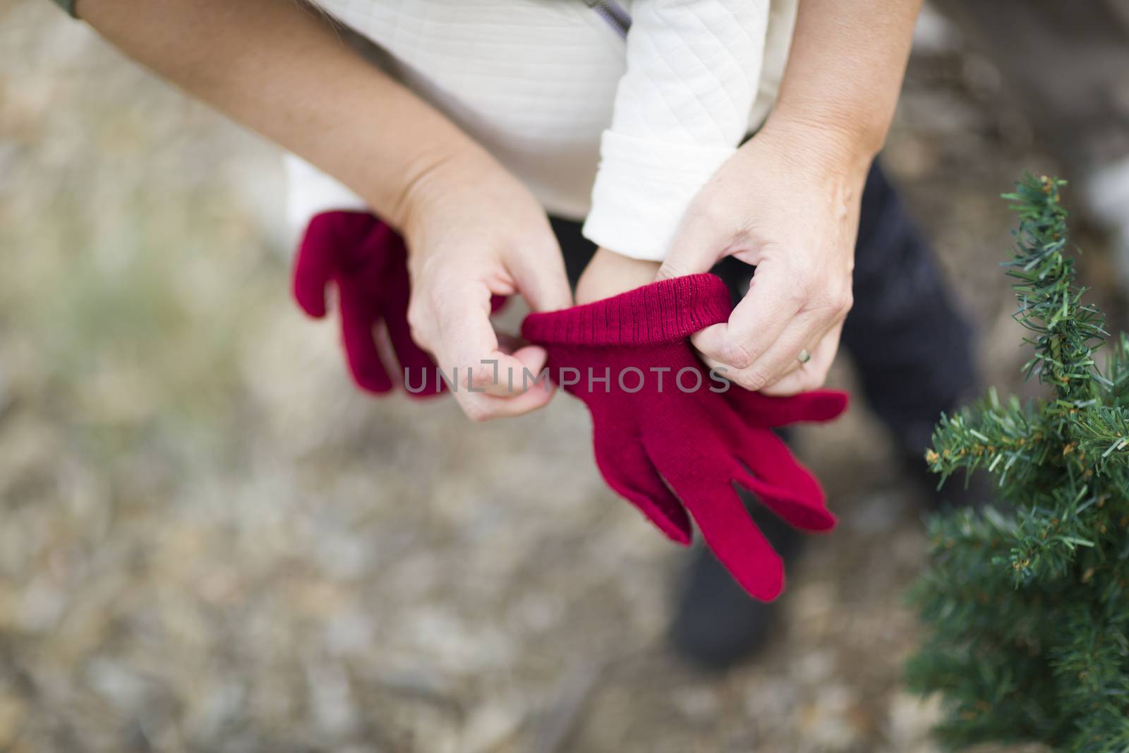 Caring Mother Putting Red Mittens On Child Near Small Christmas Tree Abstract.