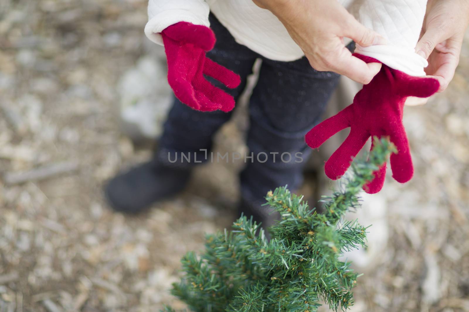 Caring Mother Putting Red Mittens On Child Near Small Christmas Tree Abstract.