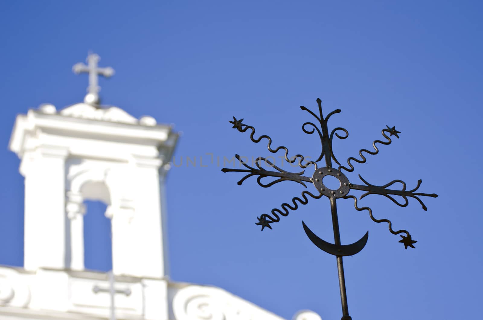 Closeup of black metal ornamental cross with a white church in the background