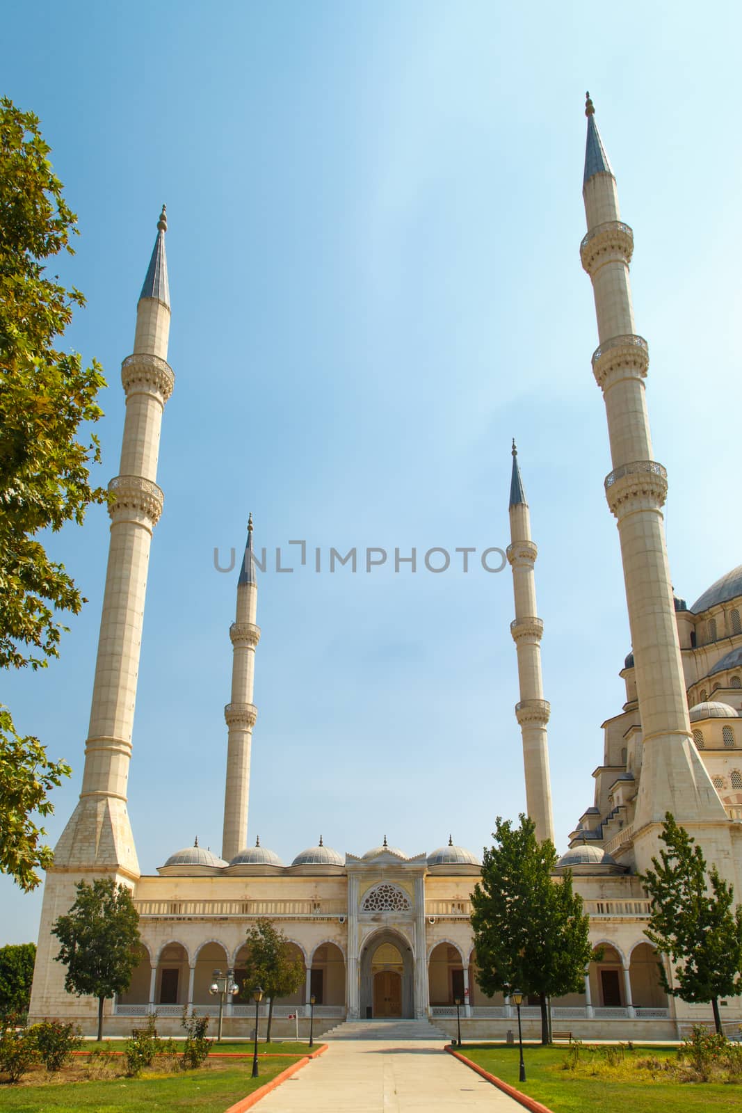 Exterior front view of Adana Sabanci Mosque, with six minarets, on bright blue sky background.