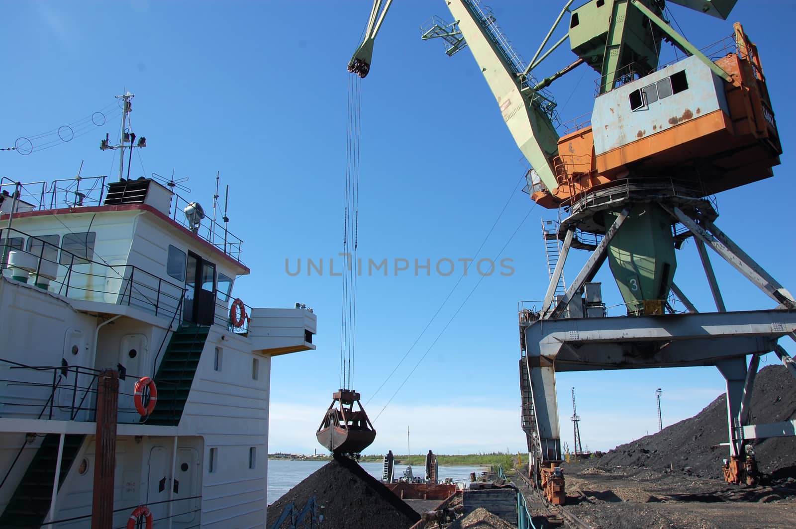 Dockside cargo crane loads coal at river port Kolyma, Yakutia, Russia