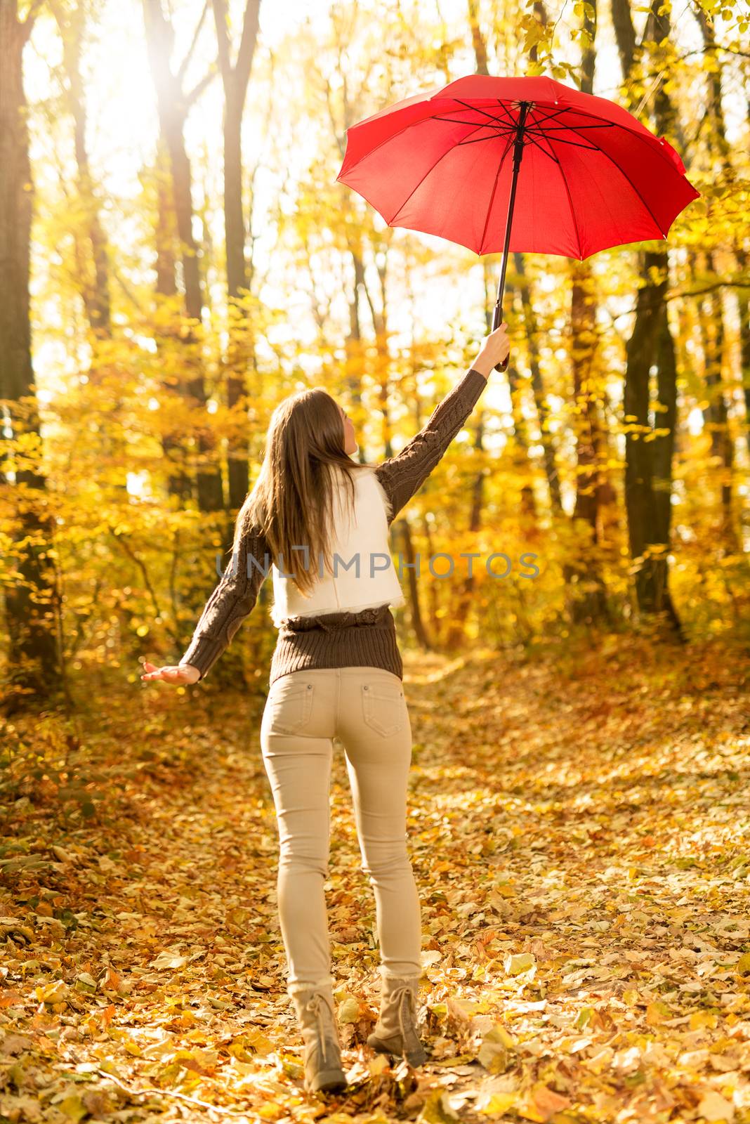 Beautiful cheerful young woman with red umbrella having fun in sunny forest in autumn colors.