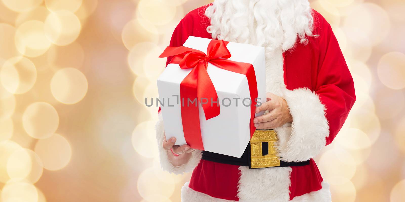 christmas, holidays and people concept - close up of santa claus with gift box over beige lights background