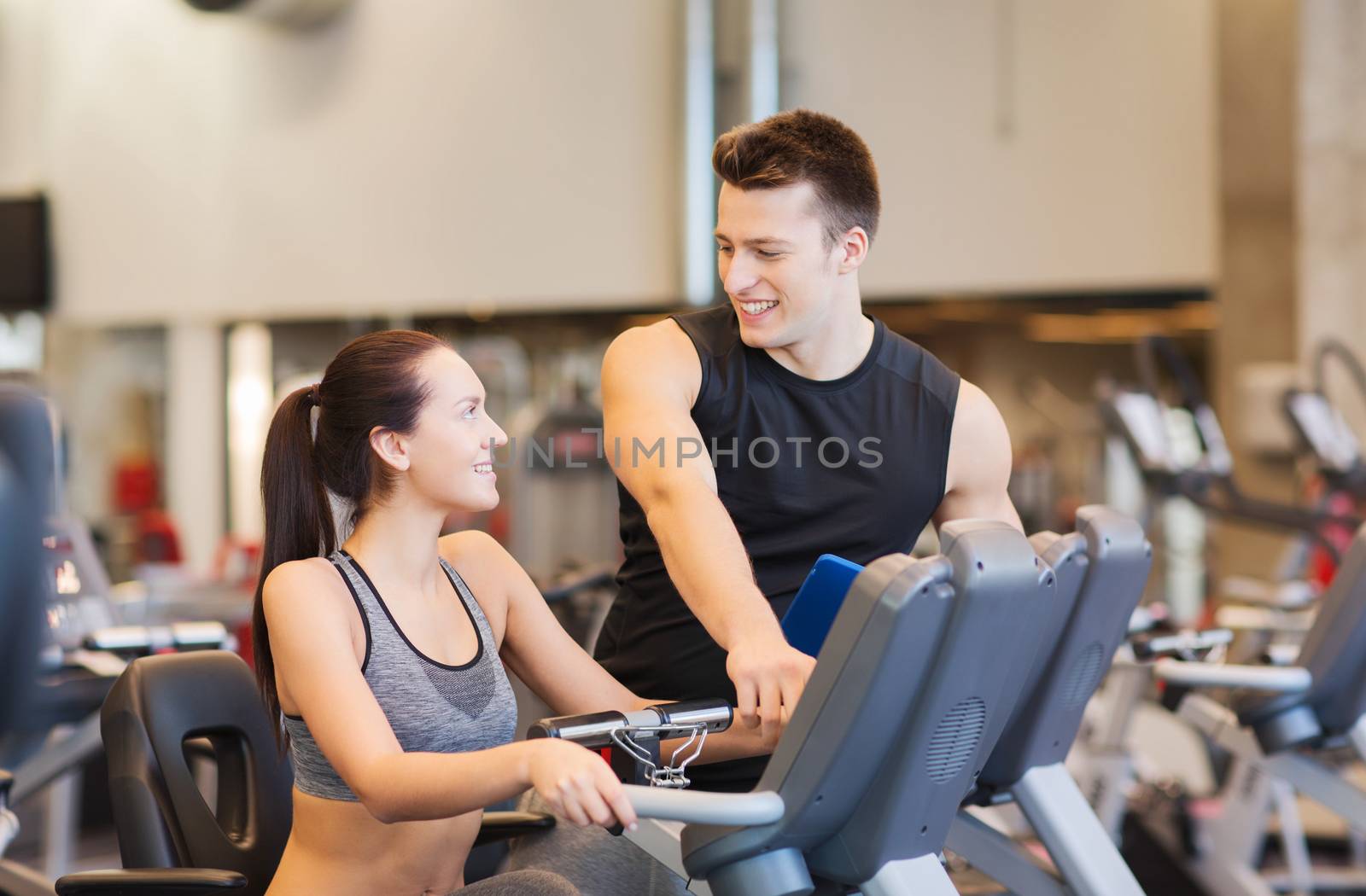 happy woman with trainer on exercise bike in gym by dolgachov