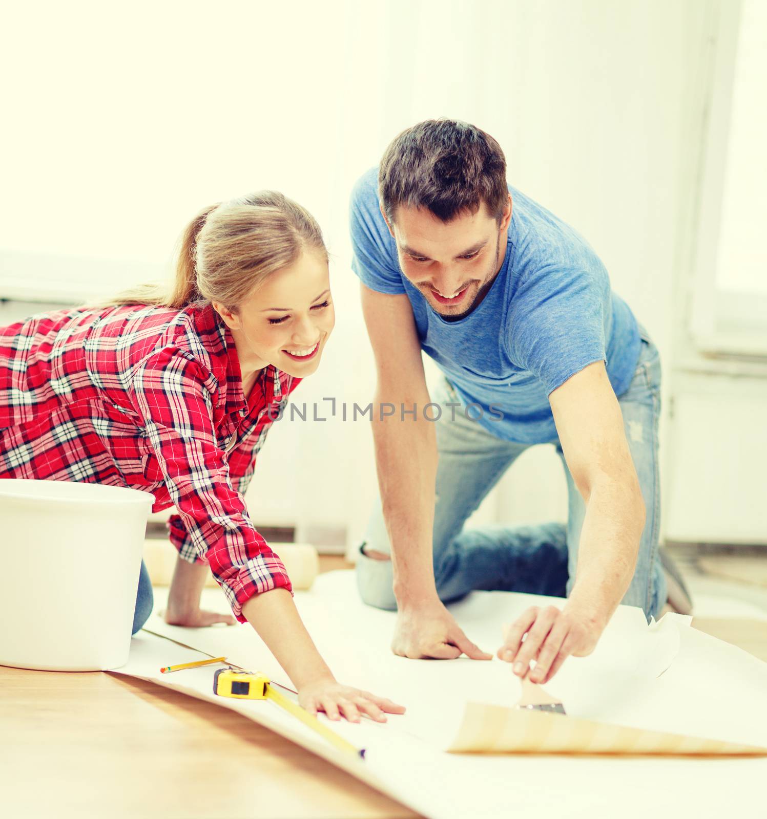 repair, building and home concept - smiling couple smearing wallpaper with glue