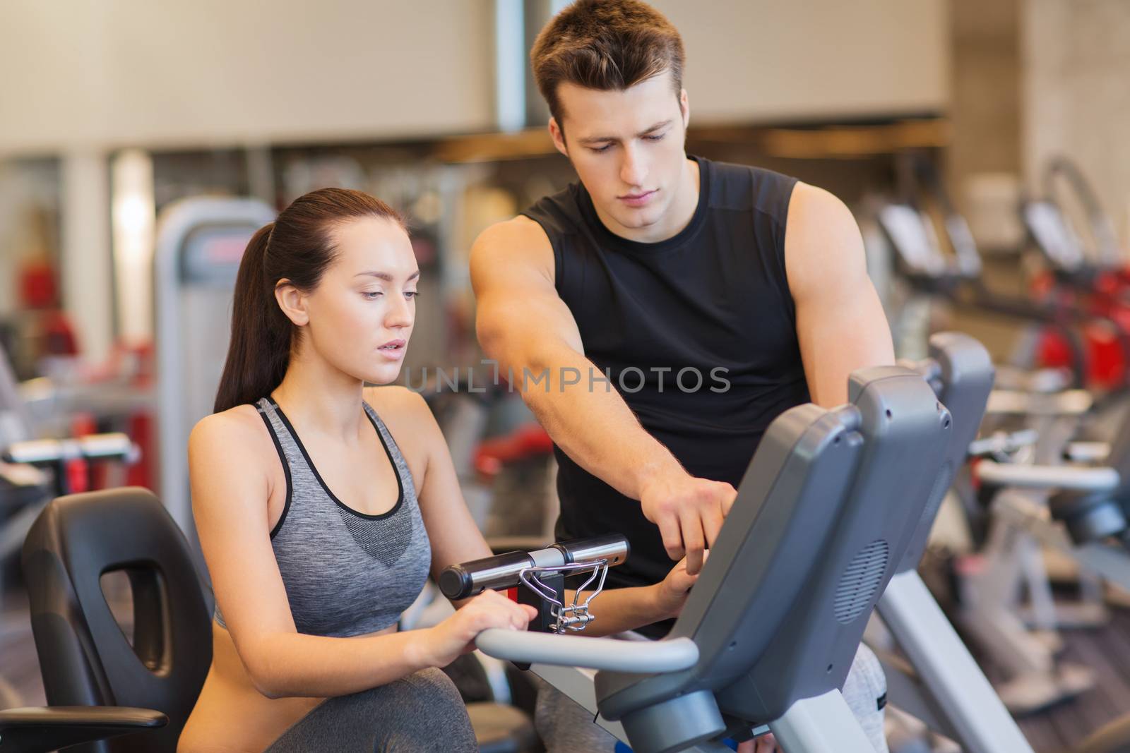 woman with trainer on exercise bike in gym by dolgachov