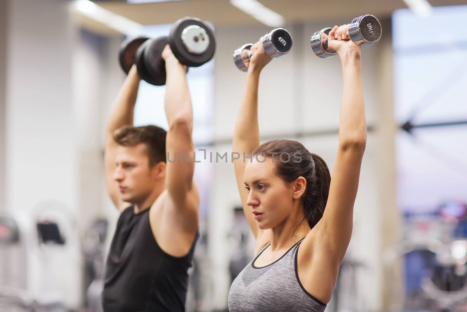 sport, fitness, lifestyle and people concept - smiling man and woman with dumbbells flexing muscles in gym