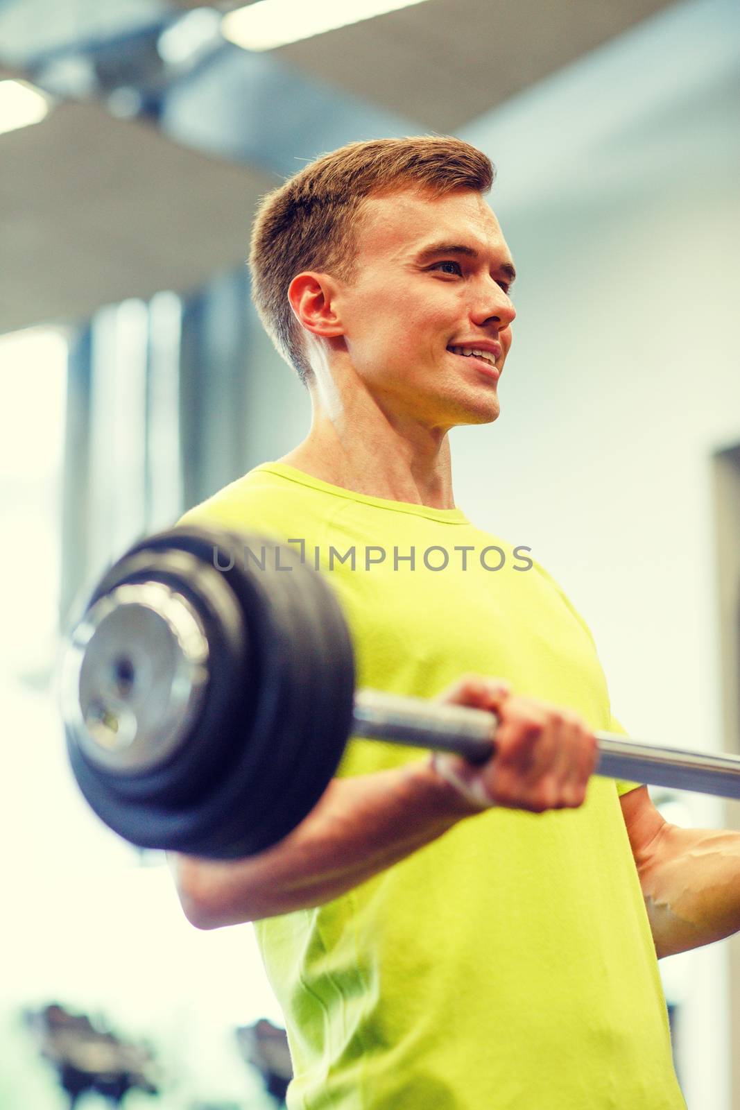 smiling man doing exercise with barbell in gym by dolgachov