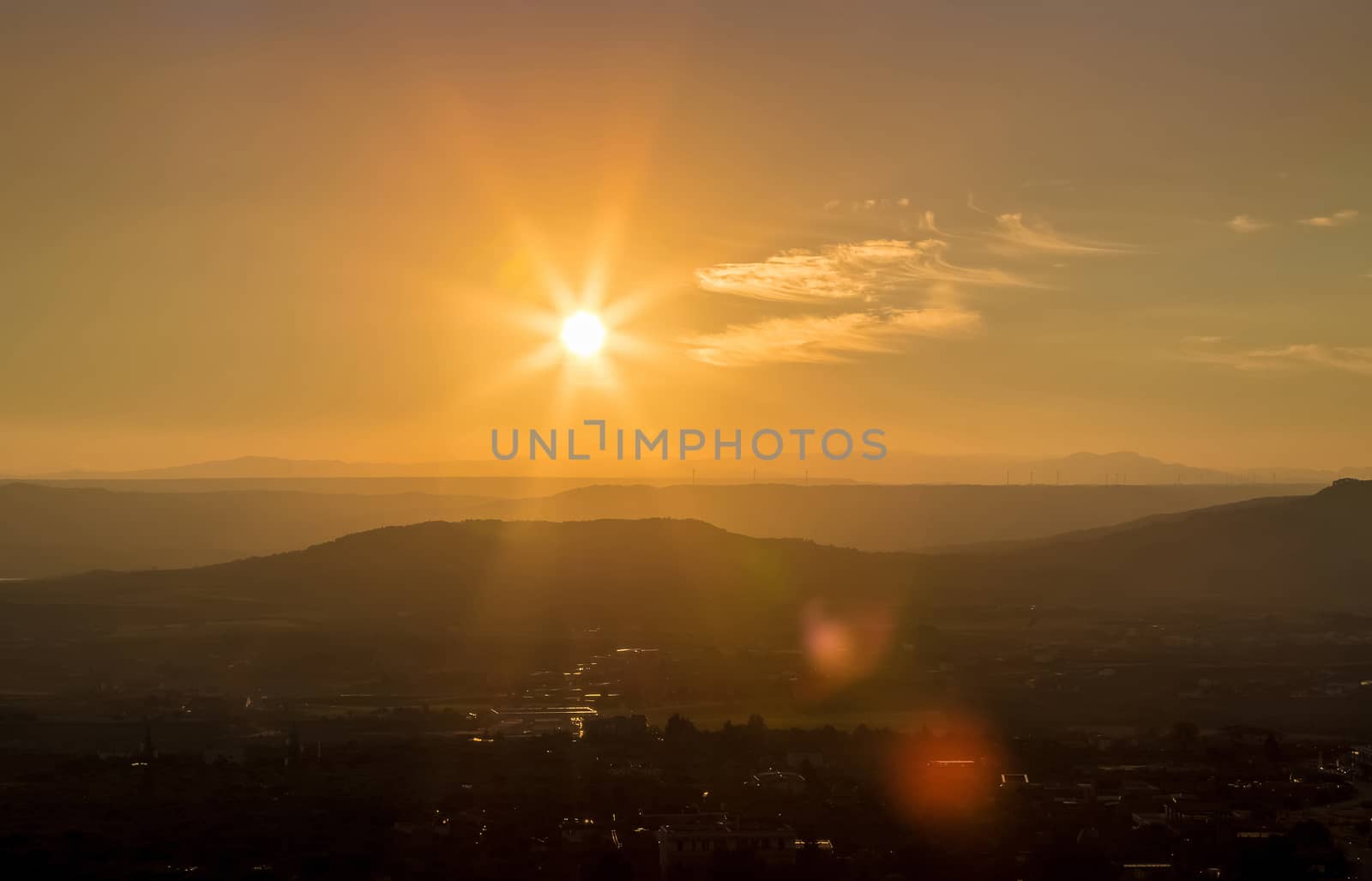 sunset scene with mountains in background, colorful sky with soft clouds and city in foreground, industrial view with sun light and lens flare