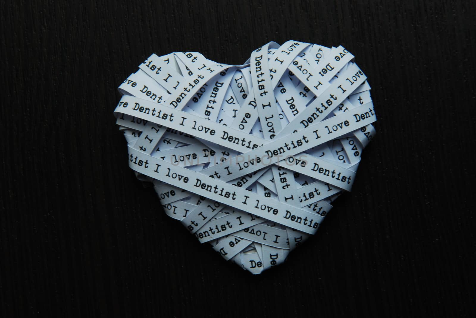 White paper ribbon in heart shape showed text 'I love dentist' on dark background by Hepjam