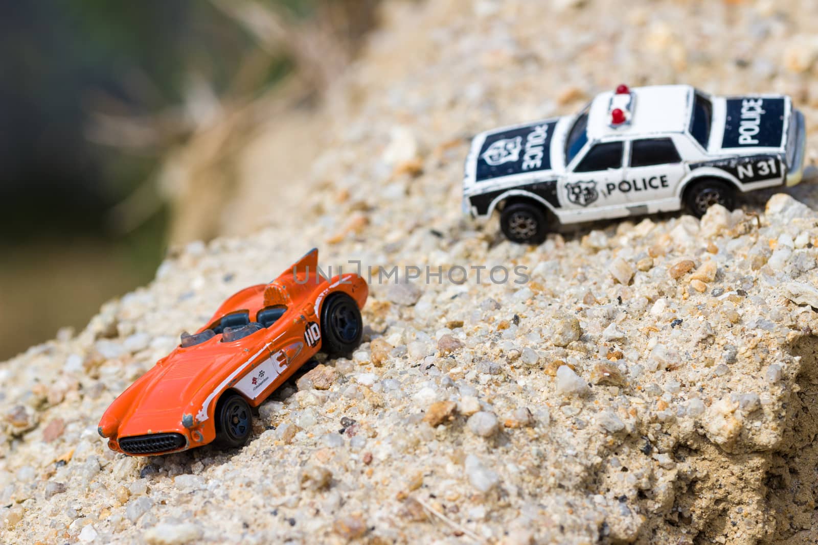 Toy cars chasing each other offroad, driving on gravel.