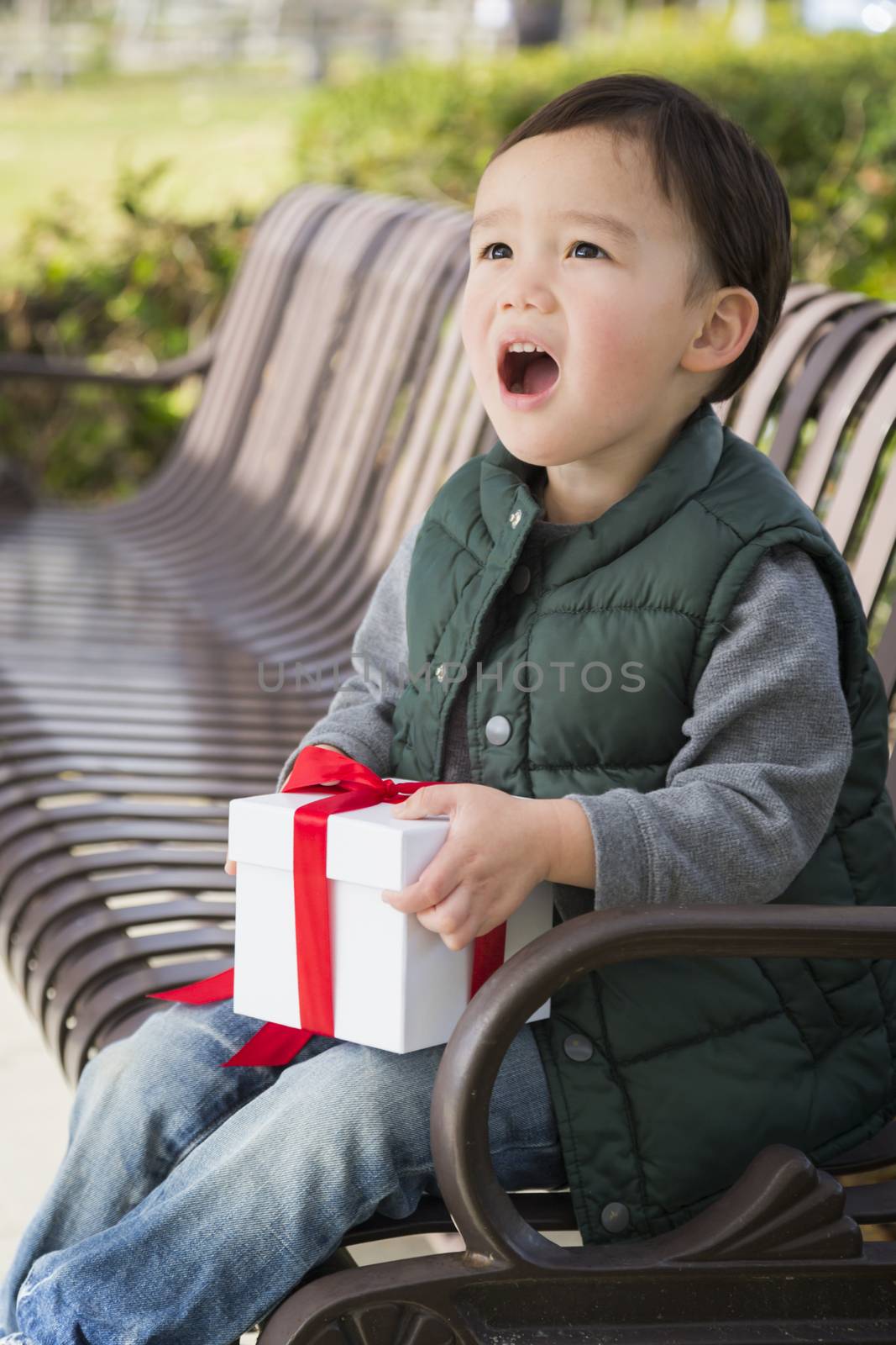 Adorable Mixed Race Boy Opening A Christmas Gift Outdoors On A Bench.