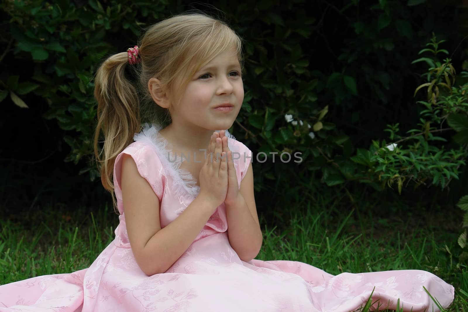 Small girl in pink dress is sitting with hands folded like in pray. by kertis