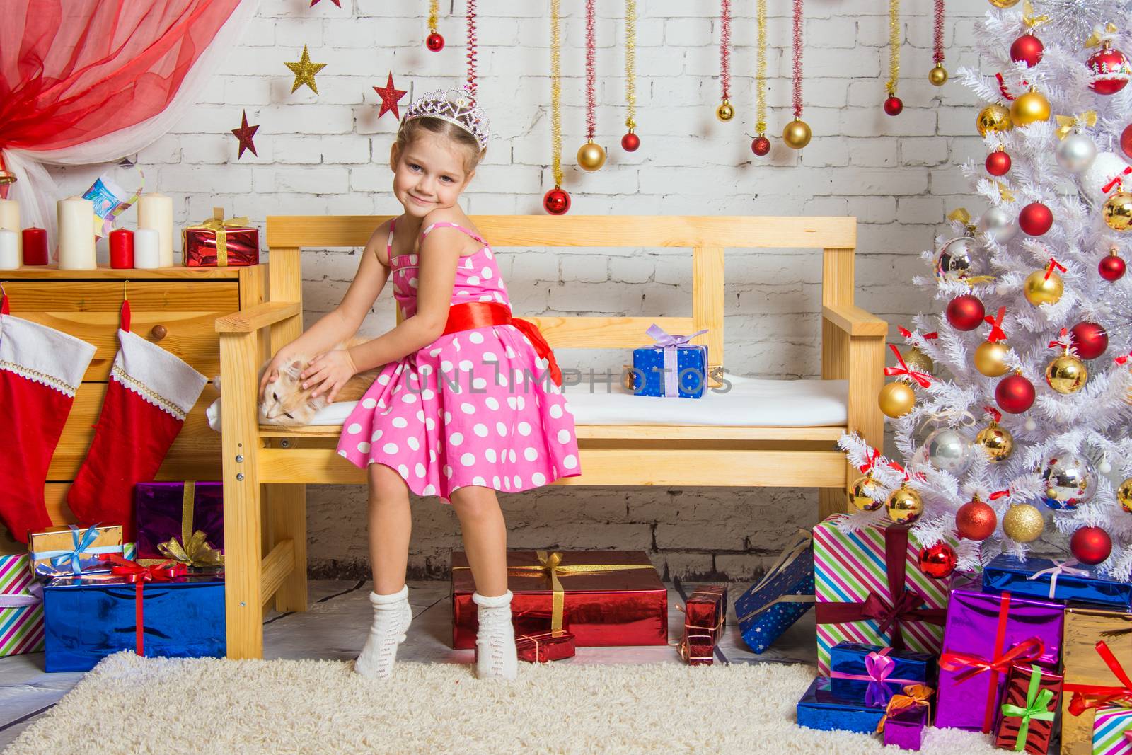 Cheerful girl four years stroking a cat sitting on a bench in the home New Years interior