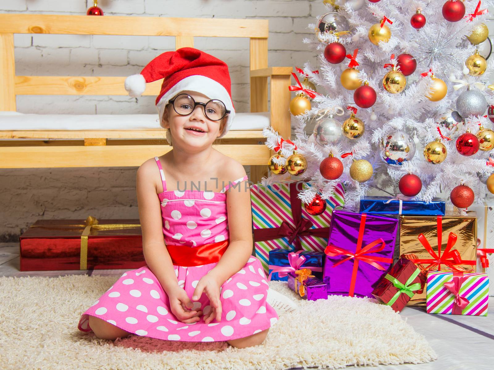 Girl in the red hat and the funny round glasses sits on a rug in the room with New Years interior