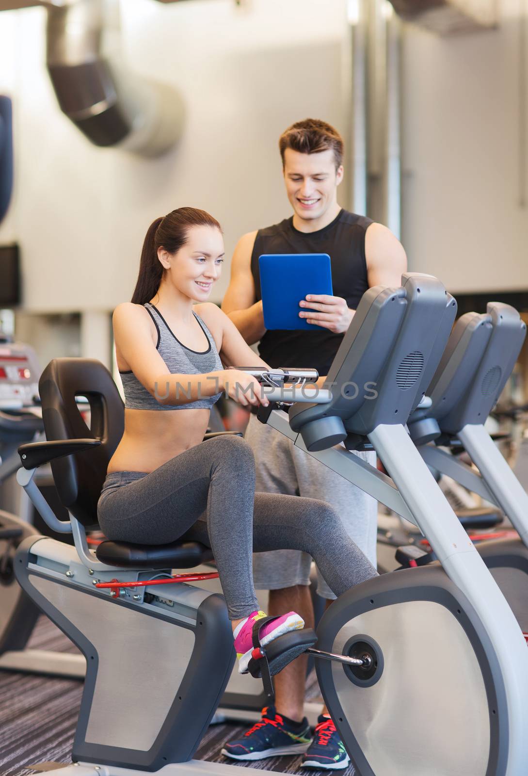 happy woman with trainer on exercise bike in gym by dolgachov