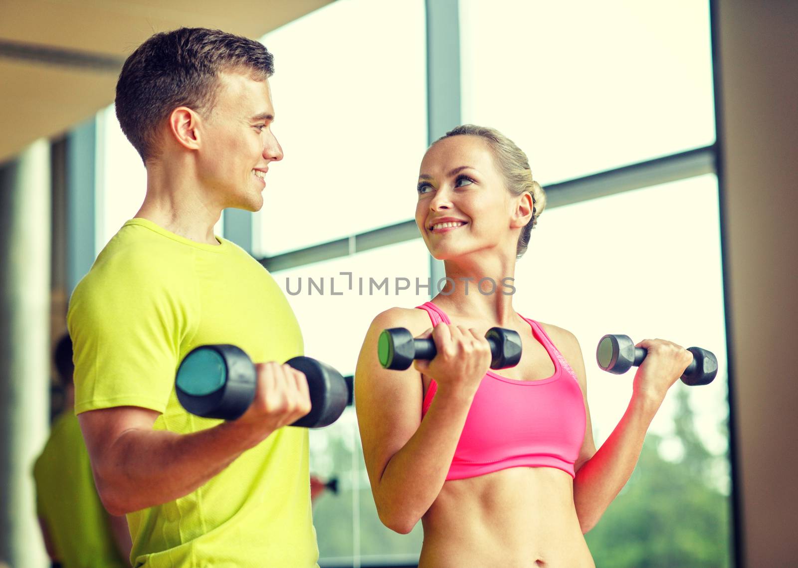 sport, fitness, lifestyle and people concept - smiling man and woman with dumbbells exercising in gym