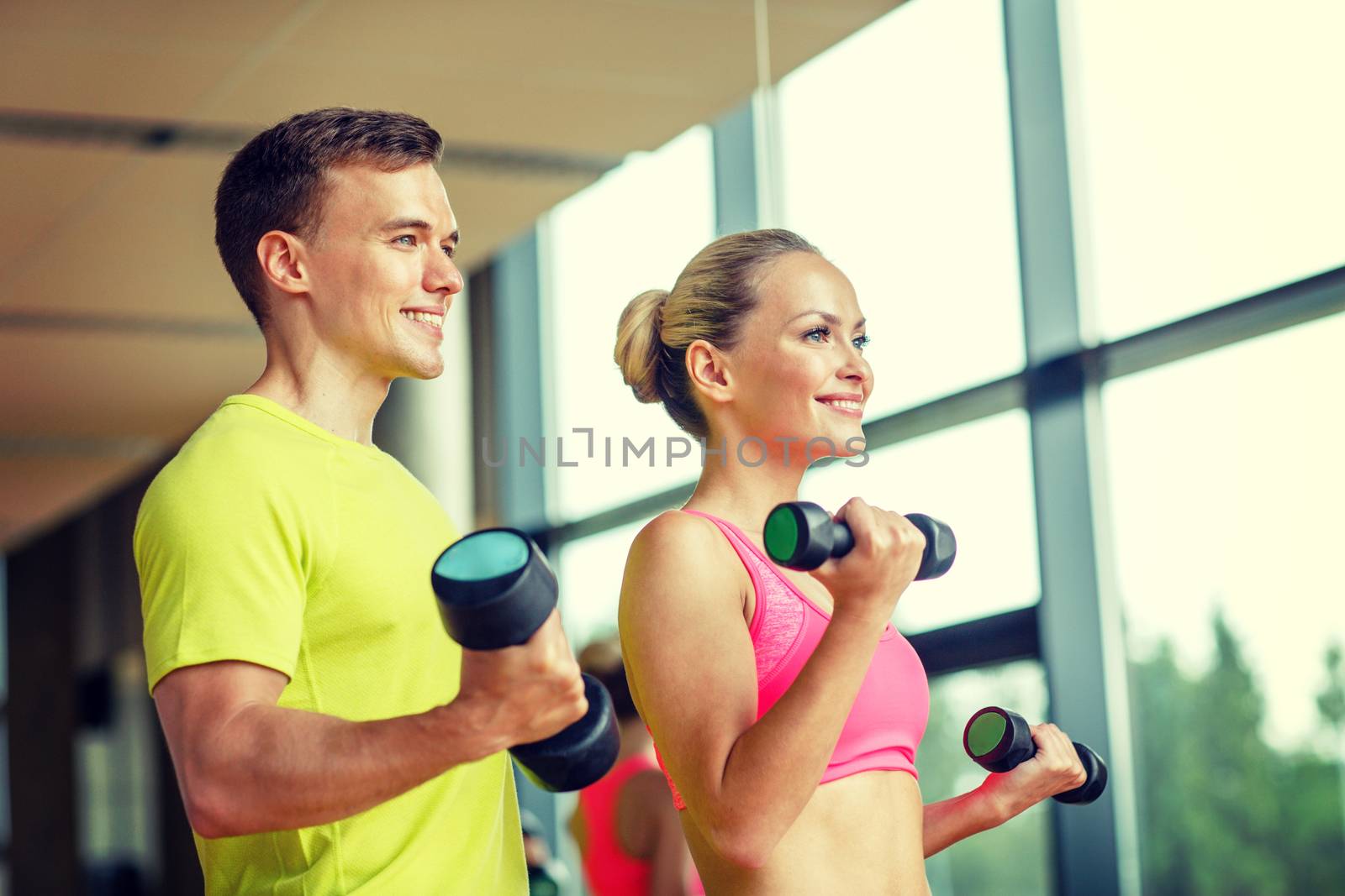 smiling man and woman with dumbbells in gym by dolgachov